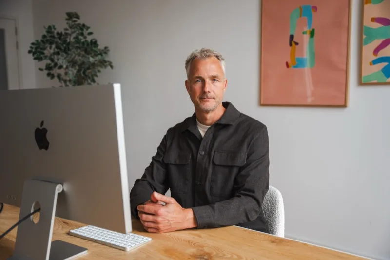 Ondernemer aan zijn bureau achter een iMac, met kleurrijke posters aan de muur